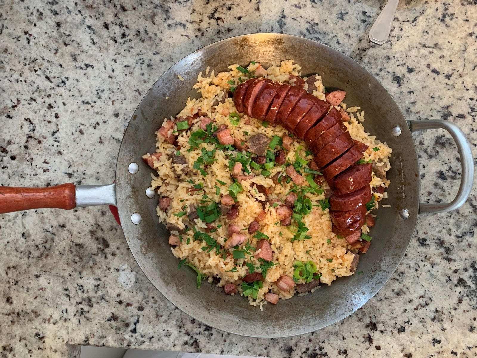 Skillet of arroz carreteiro: rice mixed with leftover beef and sliced smoked sausage, topped with green onion
