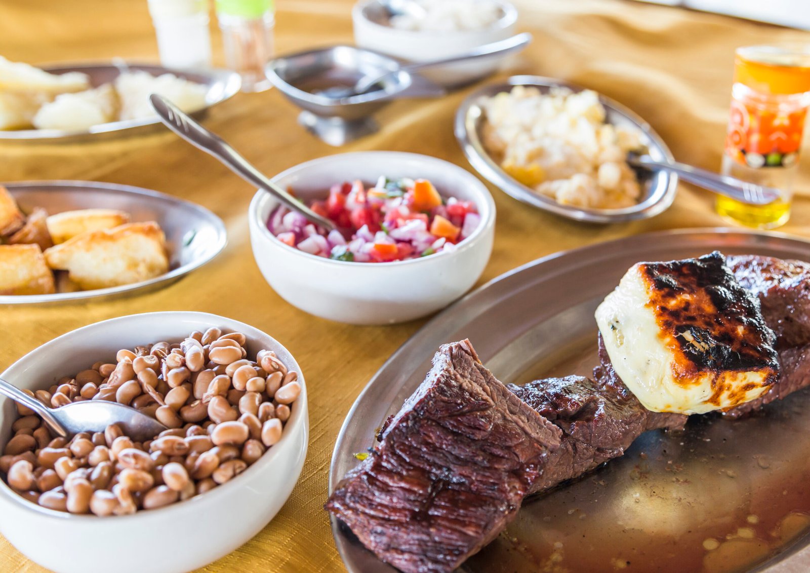Grilled carne de sol with queijo coalho, cowpeas, vinagrete and farofa on a yellow tablecloth