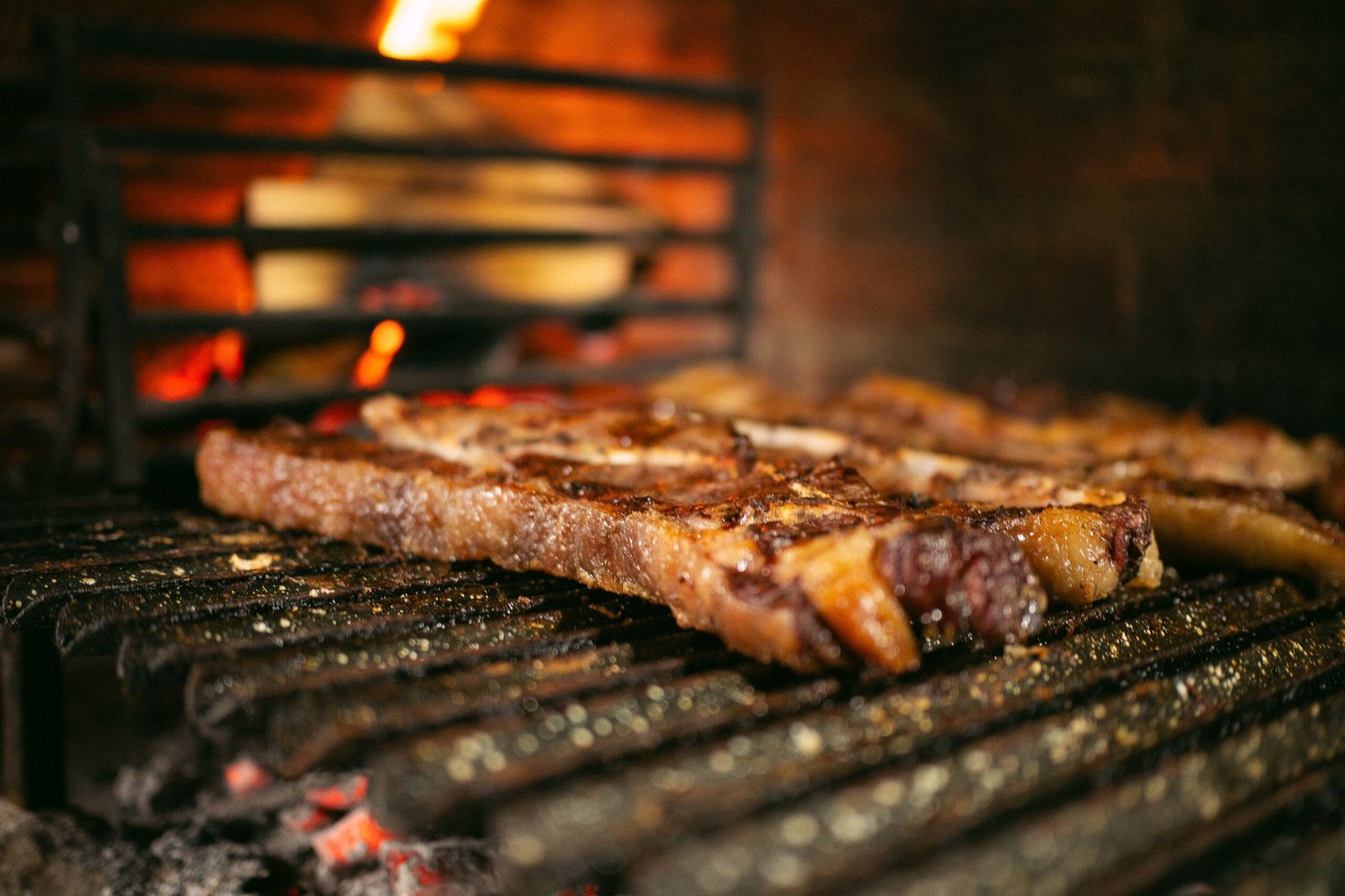 Steaks with coarse salt on a grate over glowing coals in a brick churrasqueira