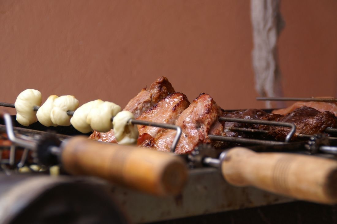 Long wooden-handled skewers with drive gears holding meat and garlic bread on a Brazilian rotisserie