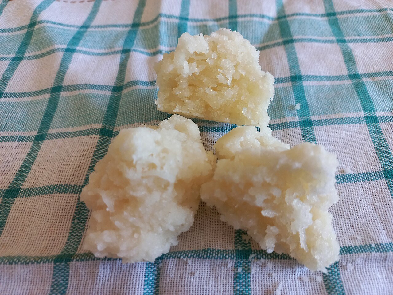 Three mounds of white Brazilian cocada, shredded coconut cooked with sugar, on a checkered cloth