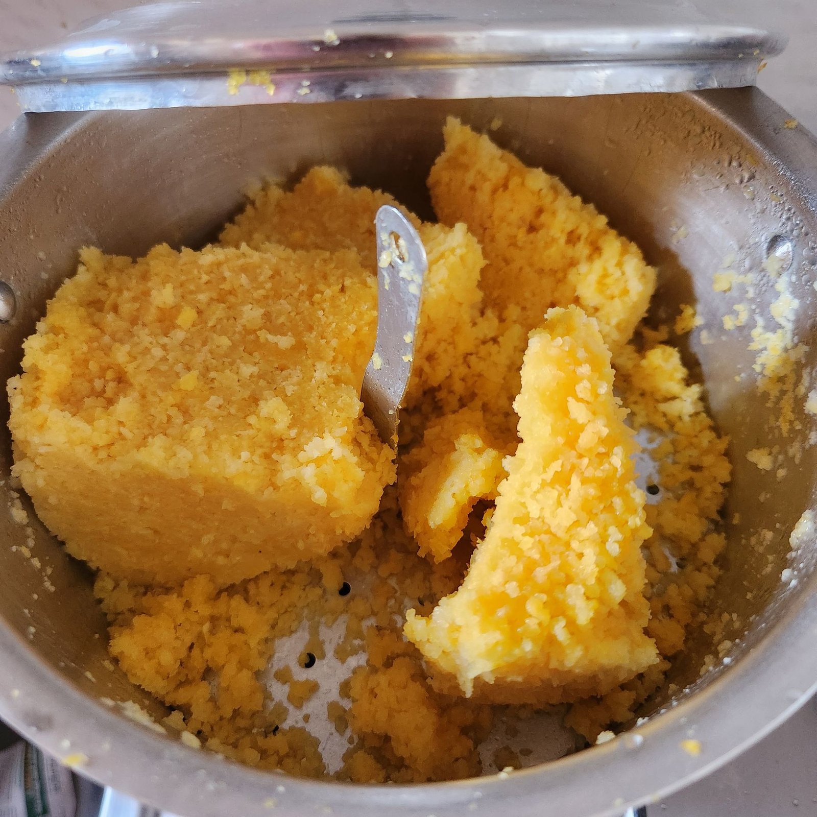 Bright yellow steamed corn couscous broken into chunks inside a metal cuscuzeiro
