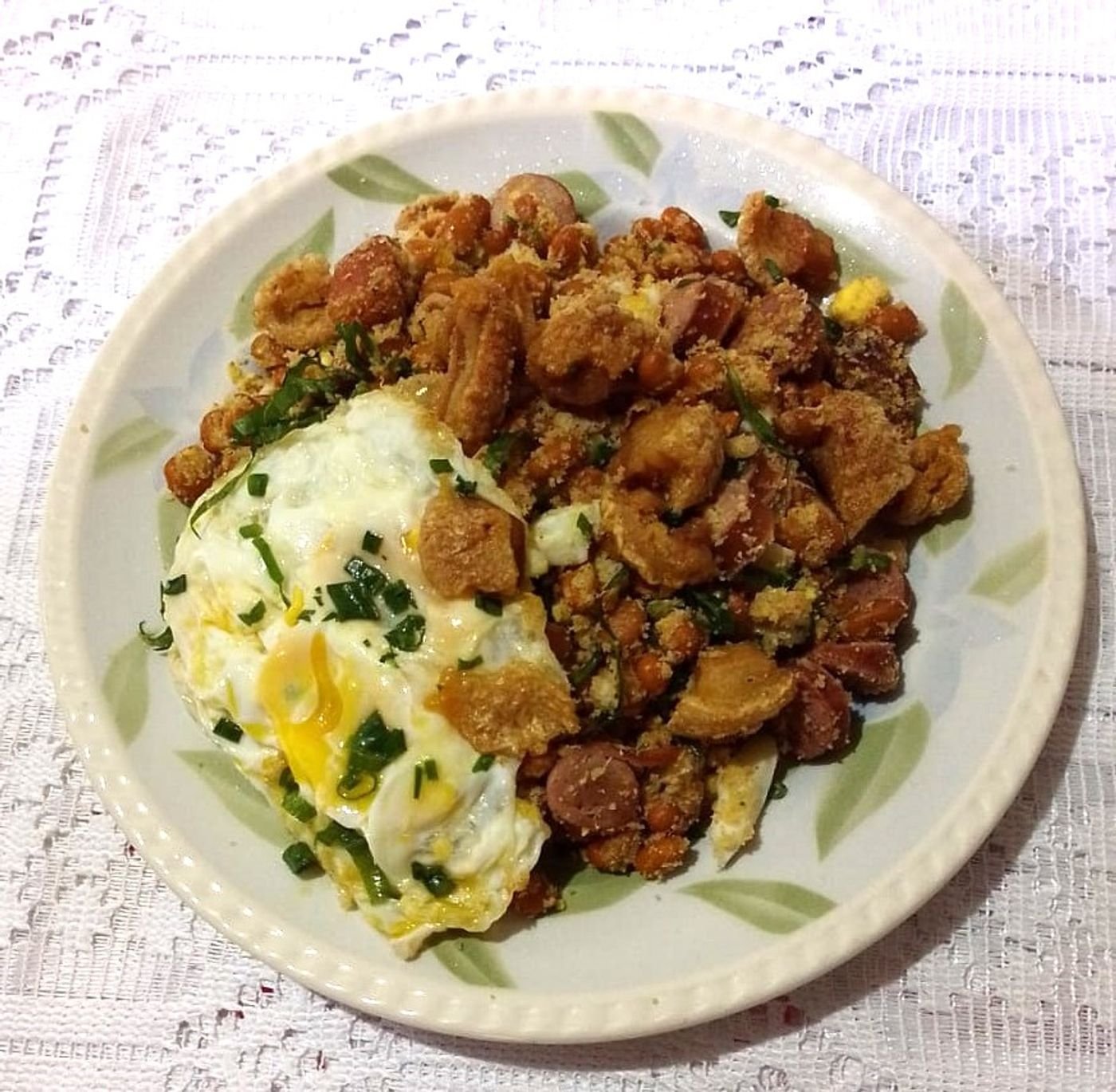 Plate of feijão tropeiro: pinto beans, cassava flour, linguiça, fried egg, and green onion