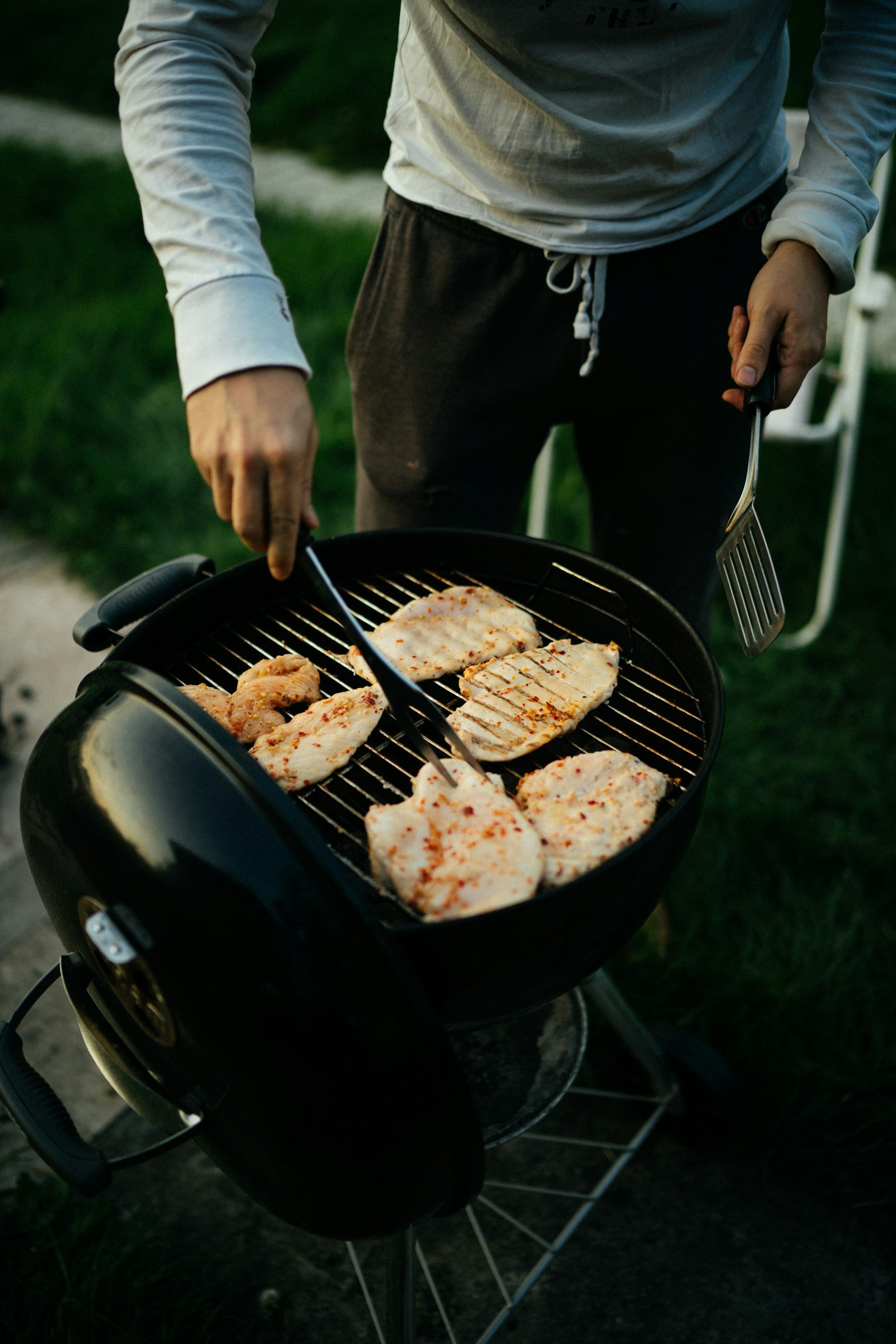 Black charcoal kettle grill with the lid open to the side and chicken on the round grate