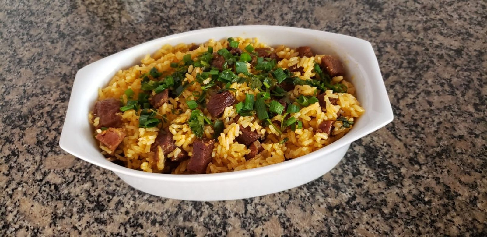 Yellow rice mixed with cubes of sun-dried beef and chopped green onion in a white bowl